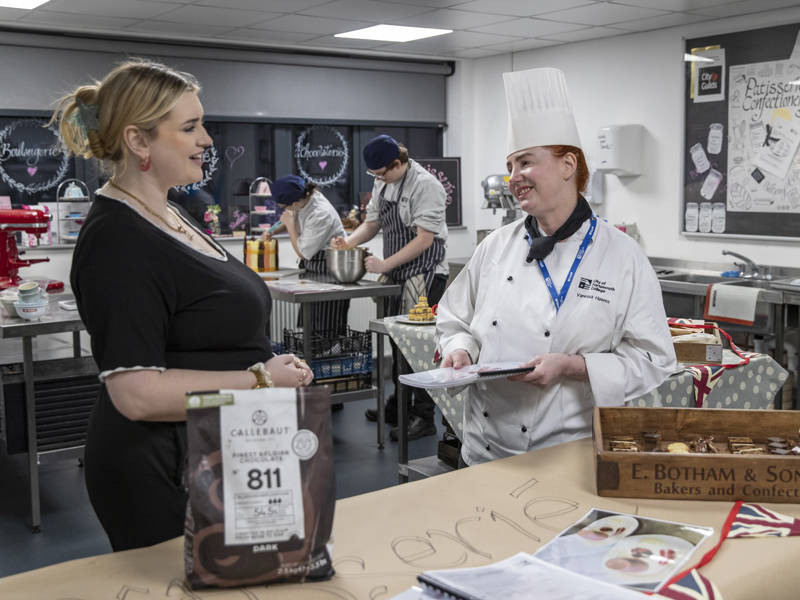 A catering lecturer chatting to a prospective student in the kitchen at City of Portsmouth College's Open Event 