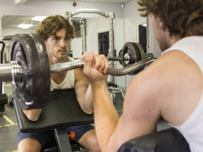 A male student lifting weights facing a mirror 