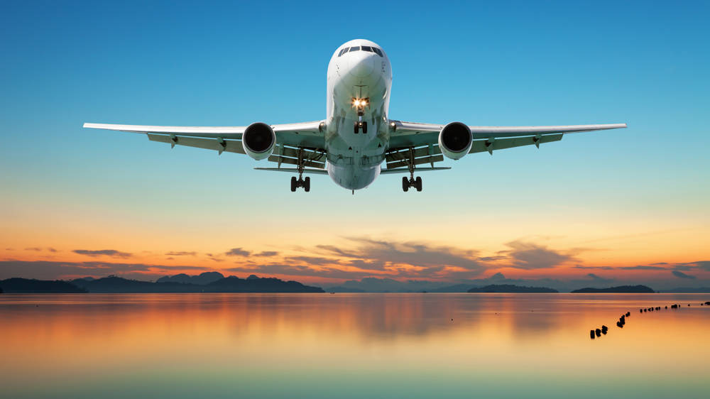 Airplane flying over tropical sea at beautiful sunset or sunrise.