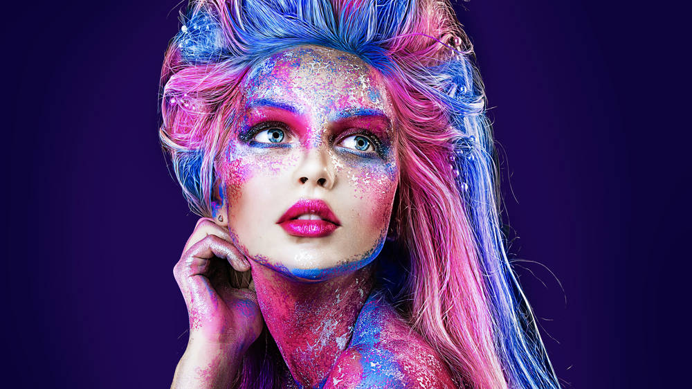 Close up portrait of young beautiful girl with colourful face painting, glitter and paint in hair.