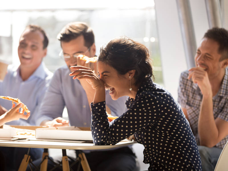 Woman laughing at funny joke with diverse coworkers in office.
