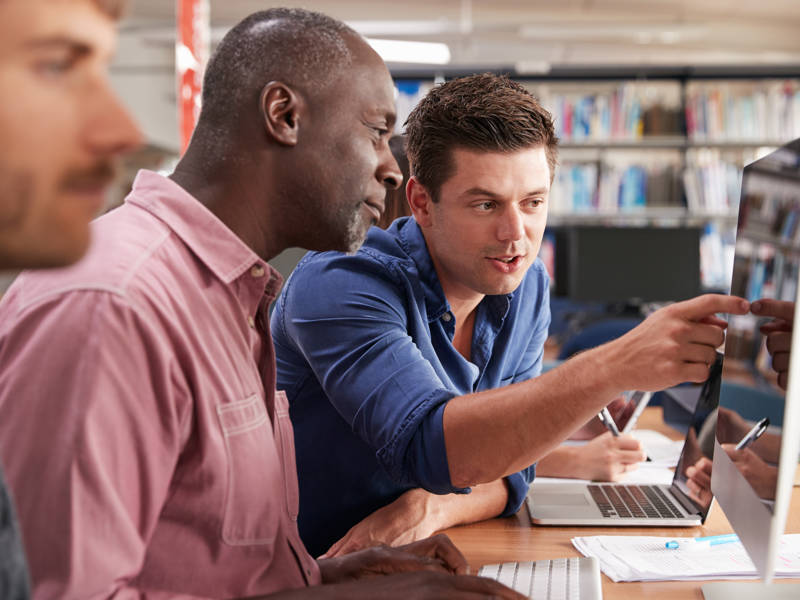 Mature Male Student With Tutor Learning Computer Skills.