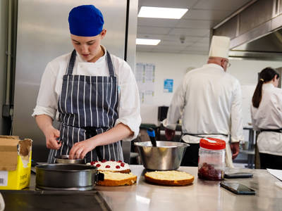 A student adding decorations to a cake in a commercial kitchen 