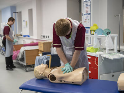 A healthcare student performing CPR on a dummy model 