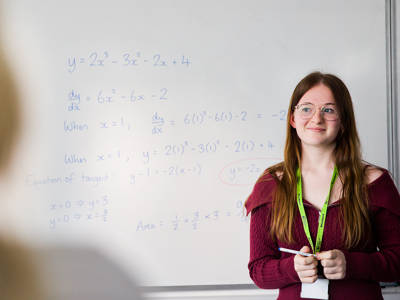 Student standing beside a whiteboard with worked maths equations and calculations.