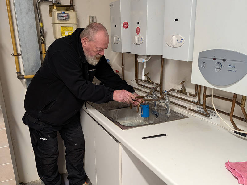 Engineer carrying out water temperature testing at sinks and water heaters during Legionella risk assessment training.