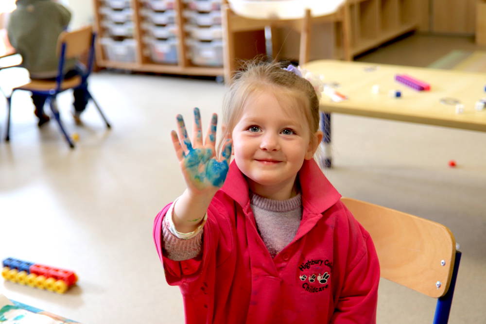Nursery pupil holds up hand covered in blue paint.