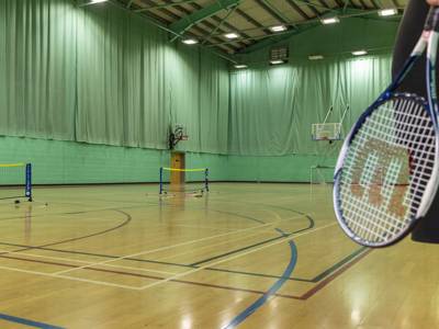 A student with a tennis racket in the sports hall at City of Portsmouth College 