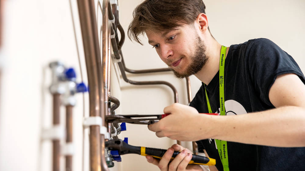 Male plumbing student working with tools in the plumbing workshop at COPC North Harbour campus