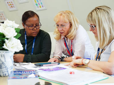 Staff member supporting adult learners while reviewing work at a table.