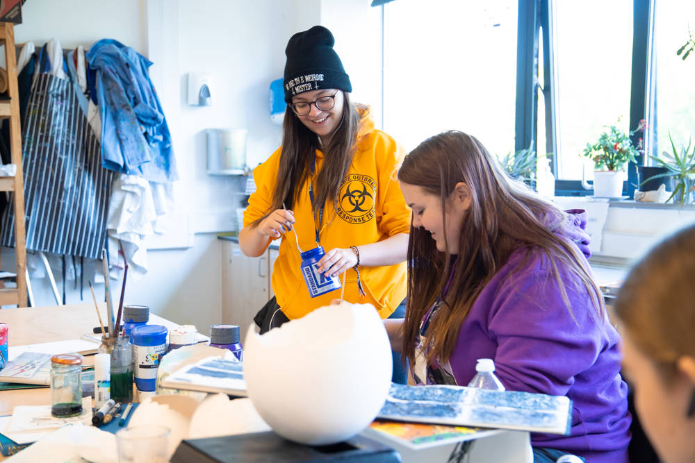 Art students smiling while working with mixed media in Art Studio.