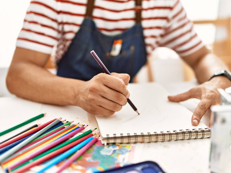 Young artist drawing in sketch book at art studio.