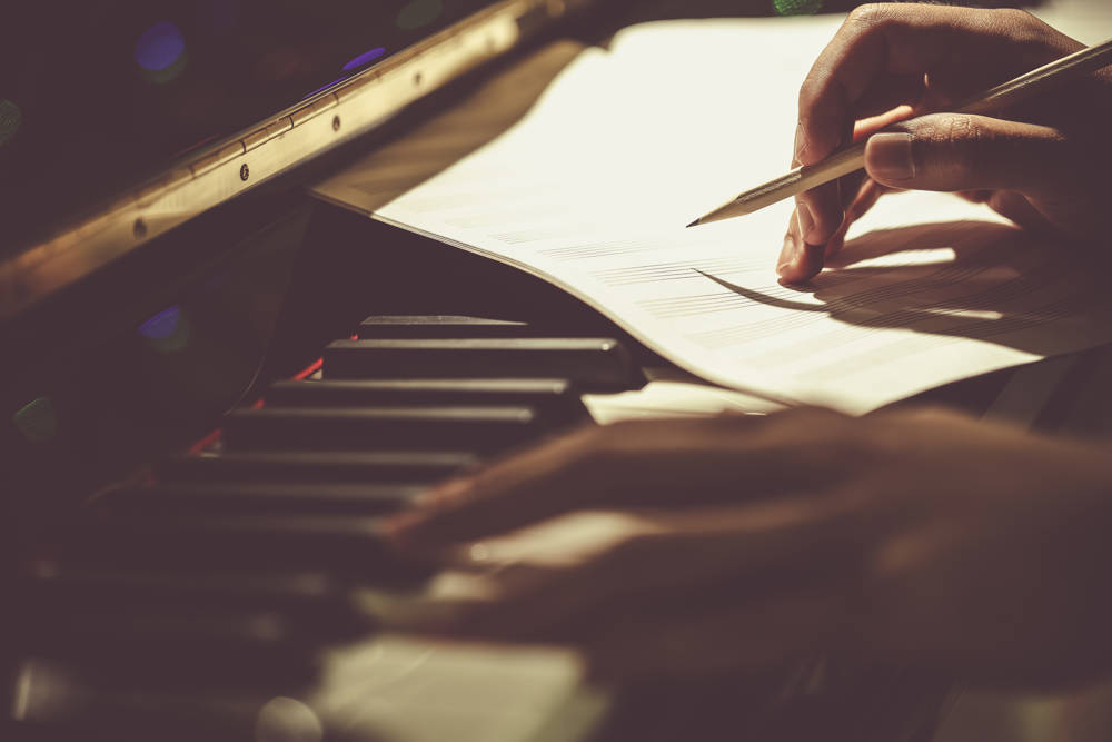 A person writing music alongside a piano 