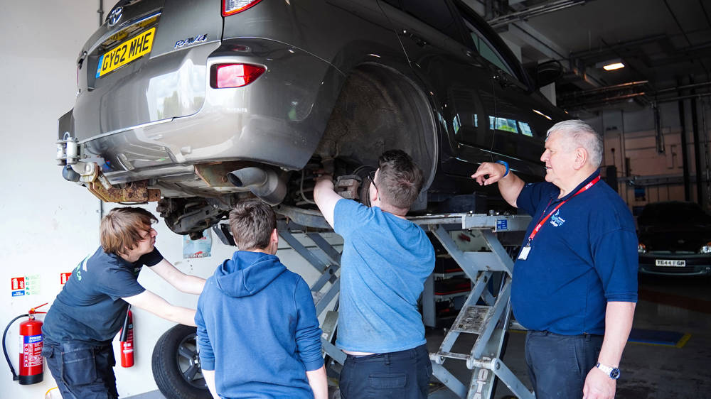 Automotive students inspect a car in the automotive workshop at Highbury Campus