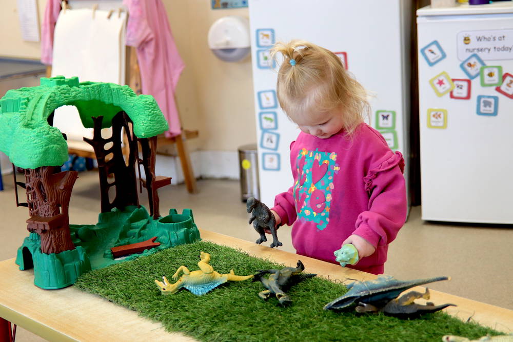 Small girl playing with toy dinosaurs at Honeypot Nursery, City of Portsmouth College.