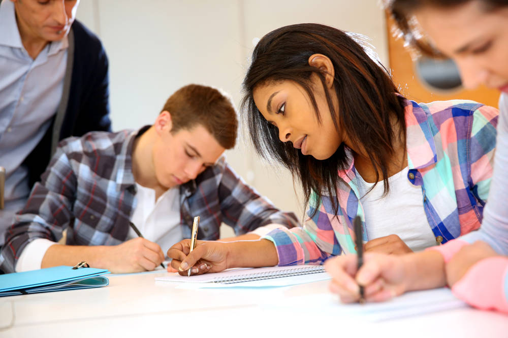 Group of teenagers in class writing their coursework